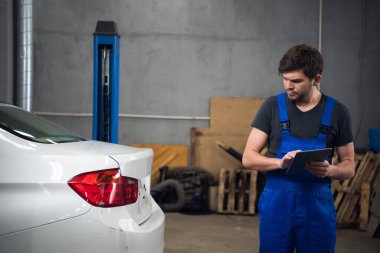 Tamirci arabayı inceliyor ve tablet kullanıyor.