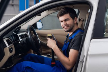 Tamirci arabanın içinde oturur ve başparmağını gösterir.