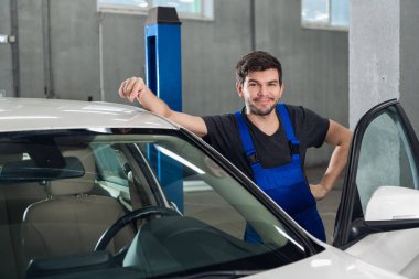 Bir tamirci arabanın yanında duruyor ve gülümsüyor.