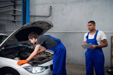 İki tamirci arabanın motorunu kontrol ediyor.