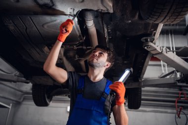 Bir makinist el feneriyle arabanın altını aydınlatıyor.