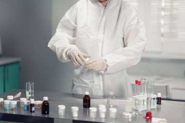 Bilimadamlarının elinde kimyasal bir numune ve çeşitli laboratuvar camları olan bir masayı tutarken çekilmiş yakın plan fotoğrafı.