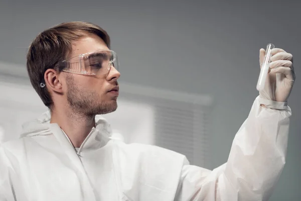 Um jovem cientista focado em óculos de proteção olhando atentamente para o precipitado em seu tubo de ensaio, um tiro de perto — Fotografia de Stock