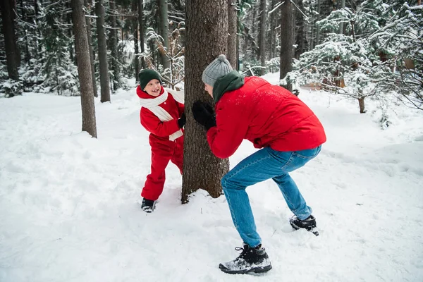 Зимой в лесу мужчина в пиджаке играет на свежем воздухе со своим сыном в комбинезоне, чтобы согреться. — стоковое фото