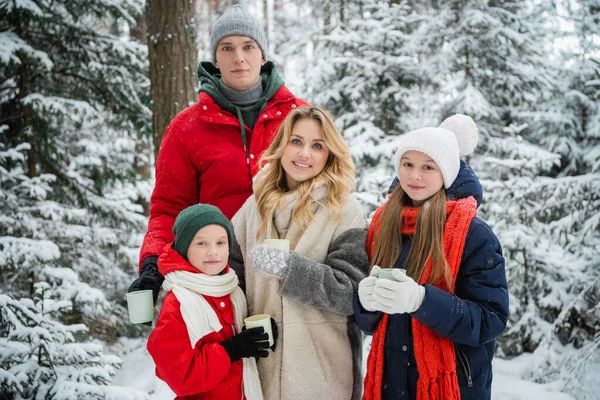 Een mooi jong stel vader en moeder met kinderen poseren voor een familiefoto tegen de achtergrond van een besneeuwd bos in een nationaal park. — Stockfoto