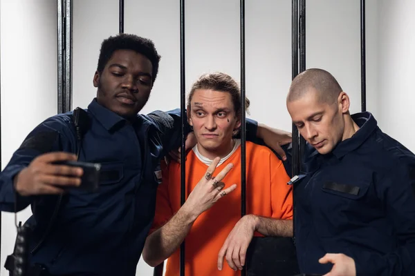 Un prisionero con tatuajes en la cara se toma una selfie con sus compañeros guardias de prisión en un teléfono inteligente. — Foto de Stock
