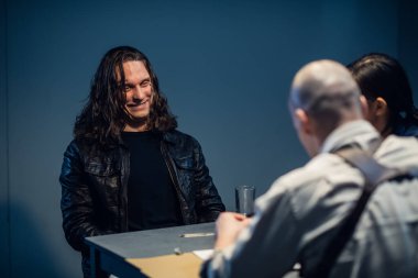 Genç polisler sorguluyor, şüpheli cesurca gülüyor.