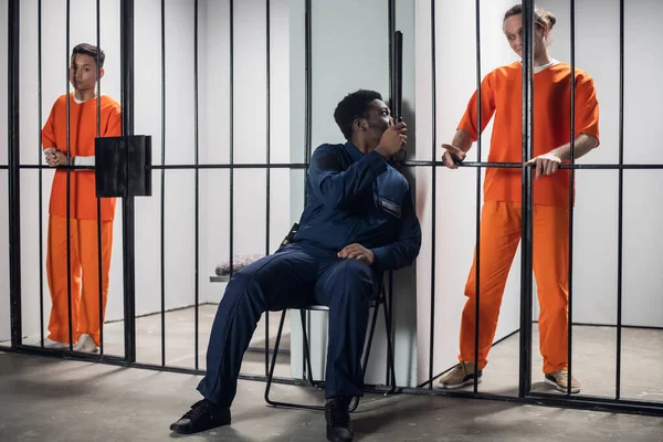 Um segurança em uma prisão de alta segurança ameaça um prisioneiro em confinamento solitário com violência física. Enredo multi-étnico na prisão. — Fotografia de Stock