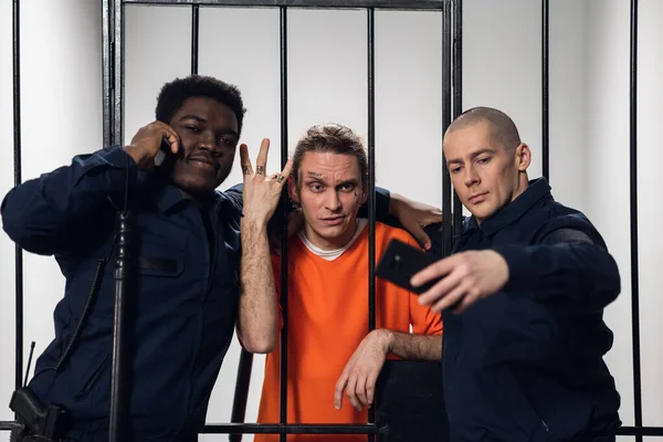 Warders in a high-security prison mock a prisoner in a cell, take photos with him on a smartphone.