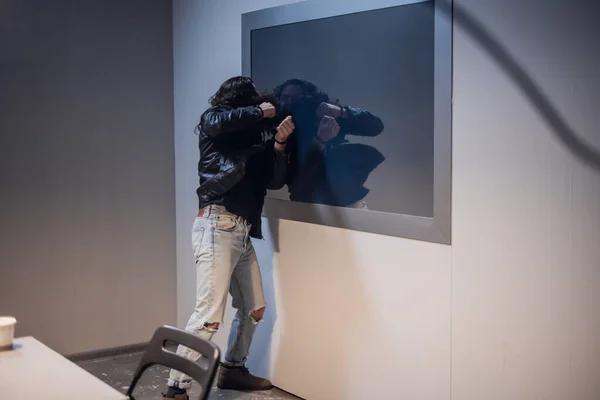 A white man with tattoos on his face tries to break the Gesell mirror in the police station interview room, because he is innocent of the crime he is accused of.