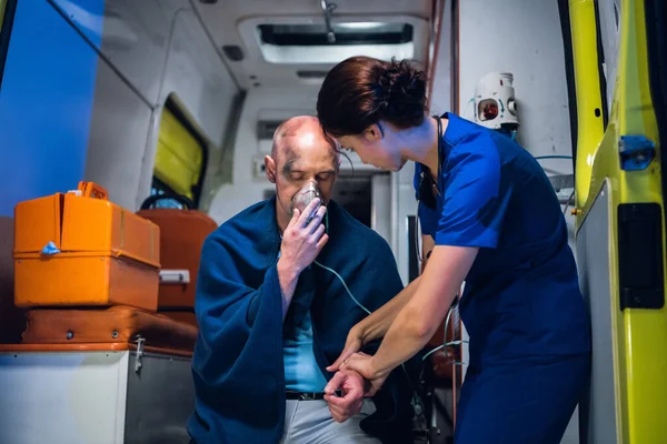 Una paramédica hembra proveyendo primeros auxilios a un hombre herido recuperado del incendio, comprobando su pulso —  Fotos de Stock