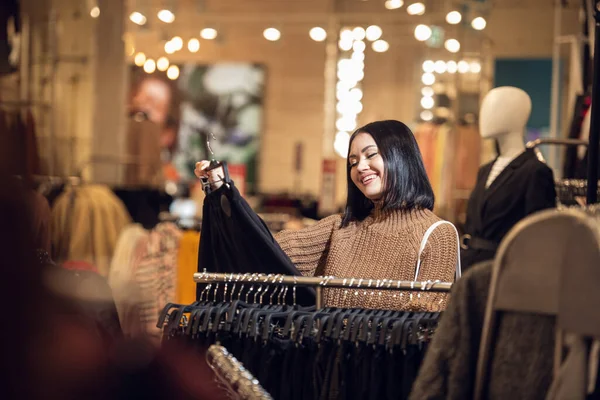 Юная улыбающаяся девушка ищет подходящую юбку в торговом центре — стоковое фото