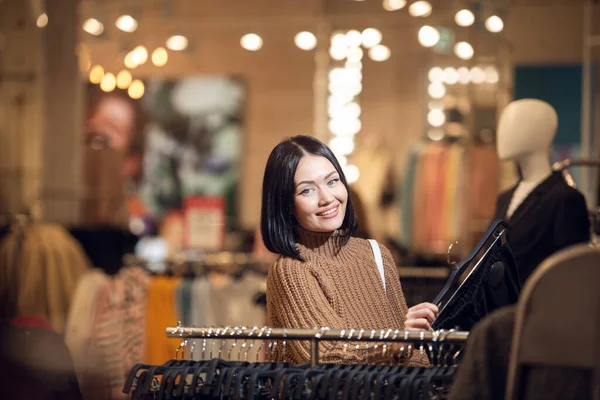 Молодая улыбающаяся девушка покупает одежду в торговом центре, смотрит — стоковое фото