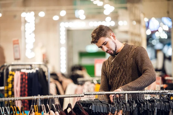 Ein junger Mann wählt Kleidung in einem Einzelhandelsgeschäft — Stockfoto