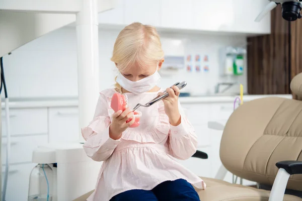 Una niña jugando con una mandíbula artificial e instrumentos médicos en una clínica dental — Foto de Stock