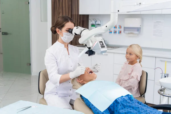 A dentist examines the oral cavity of her patient on the dentists chair with the help of a special medical appliance — Stock Photo, Image