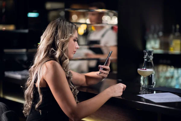 Belle fille au bar au bar écrit un message dans son smartphone — Photo