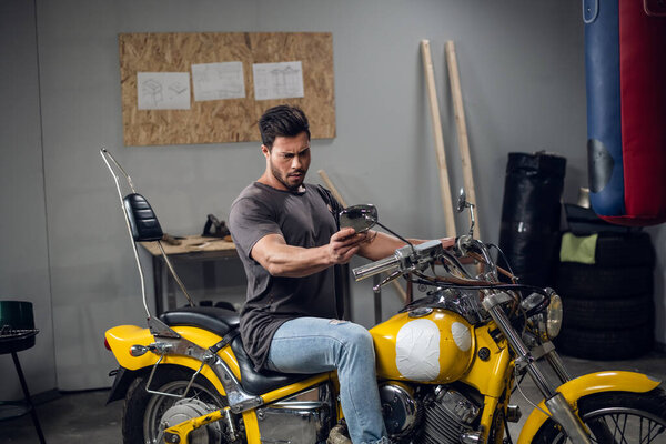 A brutal biker buys a yellow powerful motorcycle. He checks it in the garage.