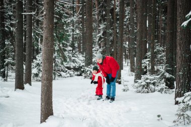 Kışın, ormanda, ceketli bir adam oğlunu sıcak tutmak için açık havada oyun oynar.