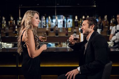 Genç sarışın bir kadın ve başarılı bir adam bir restoranda barda konuşuyorlar, kokteyl içiyorlar.