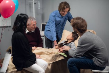 Hastane koğuşunda yatmakta olan güzel, küçük bir kızı ziyaret eden bir aile, resmi kapat.