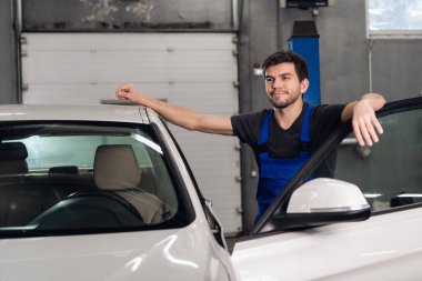 Yakışıklı bir tamirci arabanın yanında duruyor.