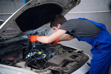 Bir işçi lamba kullanarak bir arabanın motorunu kontrol eder.