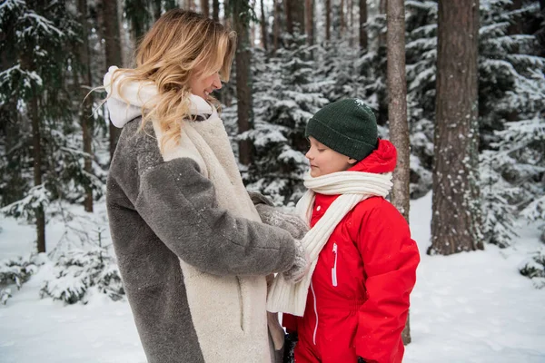 Cute blonde mom takes care of her son in the winter in the forest, they talk