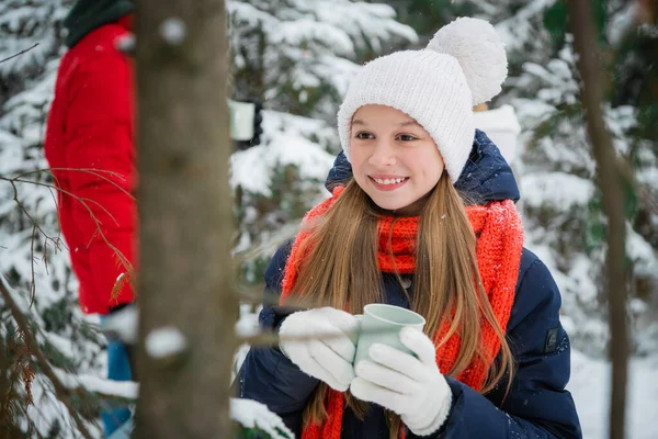 Счастливая девочка-подросток наслаждается первым снегом и пьет горячий чай из кружки в зимнем лесу во время рождественских каникул. — стоковое фото