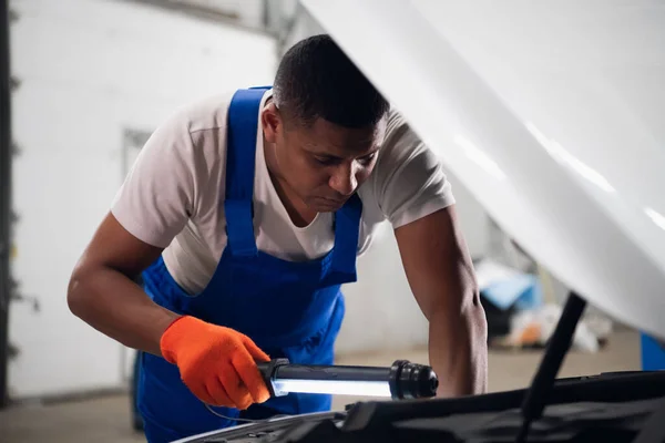 Mechanik diagnozuje silnik samochodu z latarką. — Zdjęcie stockowe