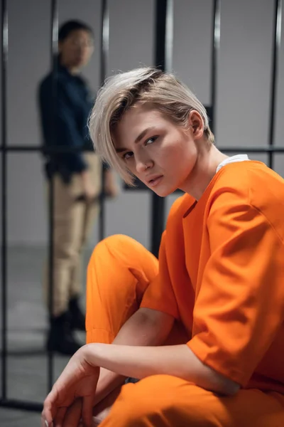 A beautiful young girl is placed under arrest in an asian prison. Sitting in a cell. In the background a female warden. — Stock Photo, Image