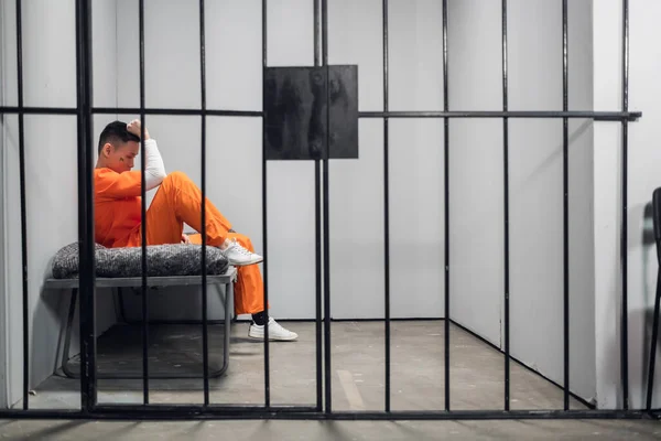 Solitary cell with a criminal in an orange robe in an asian prison. Copy space. Sad emotions of a young guy. — Stock Photo, Image