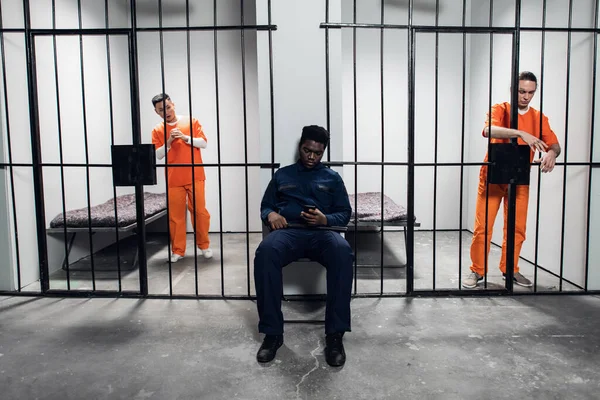 Сильний чорний охоронець охороняє клітини з в'язнями в коридорі в'язниці — стокове фото