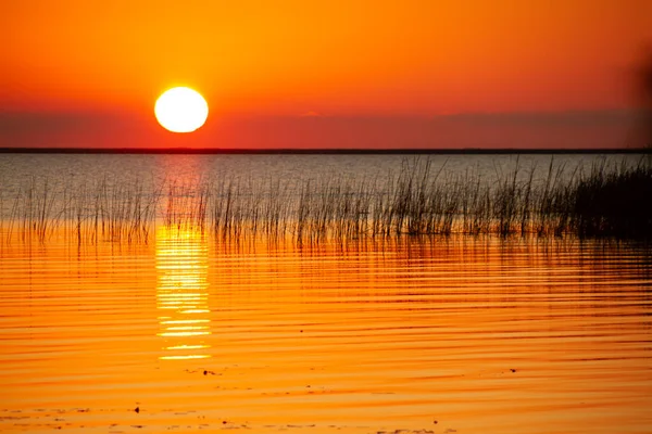 Beautiful sunset with the sun on the horizon reflecting the golden light in the lake water.