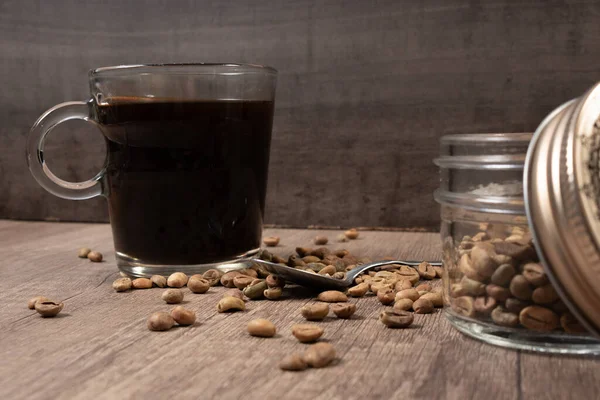 glass cup with coffee, jar with seeds, a spoon and coffee seeds on a wooden board.