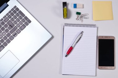Laptop, akıllı telefon ve diğer malzemelerle dolu modern beyaz ofis masası. Üst manzara, düz uzanma.