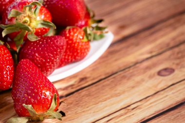 Beyaz kare bir tabakta çilekler, ahşap bir masada, kırsal bir ortamda. görünümü kapat