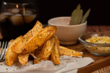 Kırsal ya da taşra usulü patates kızartması, ahşap bir tahtanın üzerinde seramik bir kasede mangal sosu ve ahşap bir masada otlu mayonez.