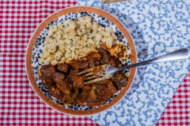 Baharatlı Macar tas kebabı spaetzle köftesi ile servis edilir, doyurucu ve lezzetli bir yemek yaratır.