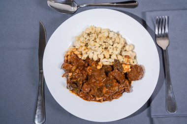 Beyaz tabakta spaetzle köfteleriyle servis edilen lezzetli Macar tas kebabı. Tadını çıkarmaya hazır.