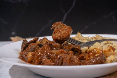 Geleneksel bir Macar yemeği olan gulaş ve spaetzle tabağından sığır eti kaldıran bir çatalın yakın çekimi.