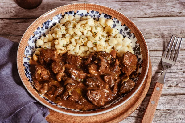 Buharda pişmiş Macar tas kebabı spaetzle köftesi ile servis edilir, doyurucu ve lezzetli bir yemek oluşturur.