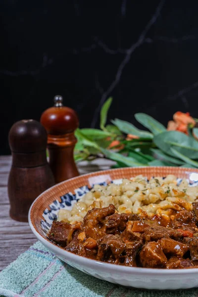 Buharda pişirilmiş Macar tas kebabı spaetzle köftesi ile servis edilir, doyurucu ve lezzetli geleneksel bir yemek oluşturur.