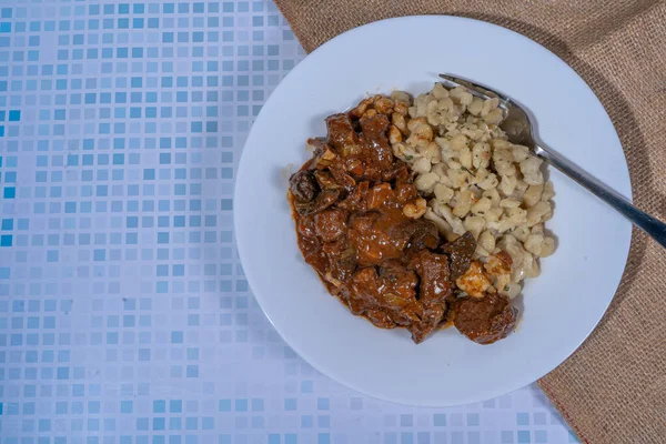 Spaetzle buharlı gulaş, lezzetli ve lezzetli bir Macar güveci, beyaz bir tabakta servis edilir, keyif almaya hazır.