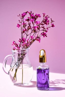 Özlü kaplıca şişesi kuru çiçekler ve pembe arka planda küçük pembe çiçekler, yakın plan, kopya alanı, cilt ürünleri, ev spa tedavisi için doğal kozmetik ürünleri