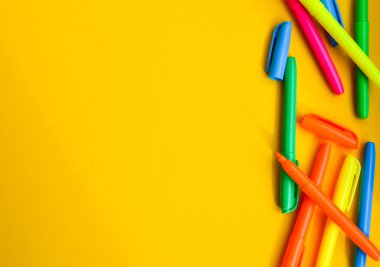 Fotokopi alanı olan sarı arka planda keçeli kalemler, kapakların yanında yeni açılmış renkli keçeli kalemler. Ofis malzemeleri konsepti