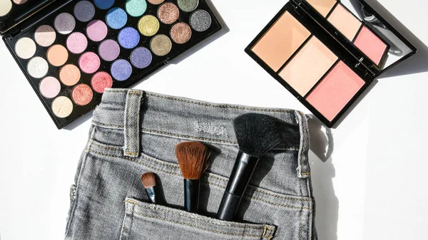 Set of woman accessories, beauty products and cosmetics on a classic gray jeans. Fashion and shopping concept. pastel colors eyeshadows and highlighter on white background