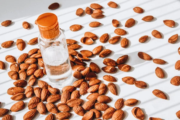 Almond nuts scattered white wooden table, bottles of culinary and cosmetic skincare seed oil, Almond essential oil, Bottle of extra virgin almonds oil, beauty concept cosmetics