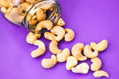 Kavrulmuş fındık yığınını kapat cam kavanozdan dökülen fındıklar mor zemin üzerine saçılmış, hammadde olarak kullanılan tropikal meyve tohumu pek çok çeşit pişirme veya atıştırma olarak yeme, sağlıklı yeme