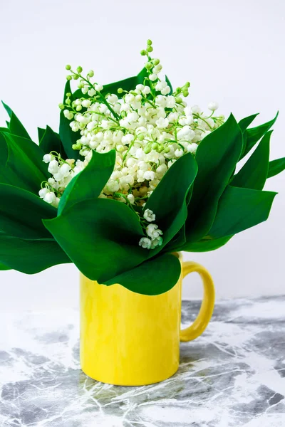 bouquet of lilies of the valley in yellow tea cup on a white table with copy space. concept of holiday background, springtime at home